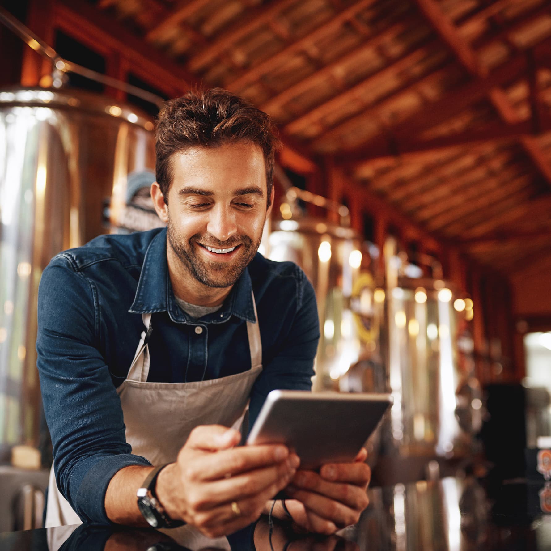 Brewery owner checking a tablet beside the brewing tanks